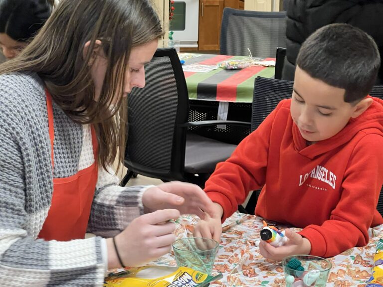A boy in a red sweatsuit making a modeling clay snowman